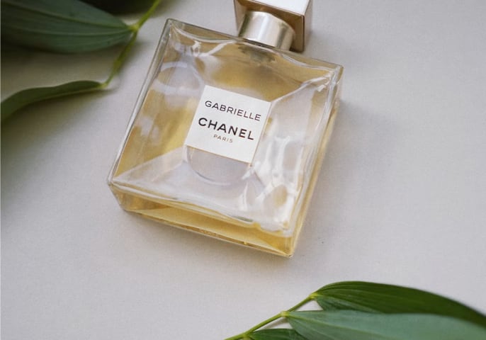 Gabrielle Chanel perfume bottle placed on a flat surface with green leaves around it.