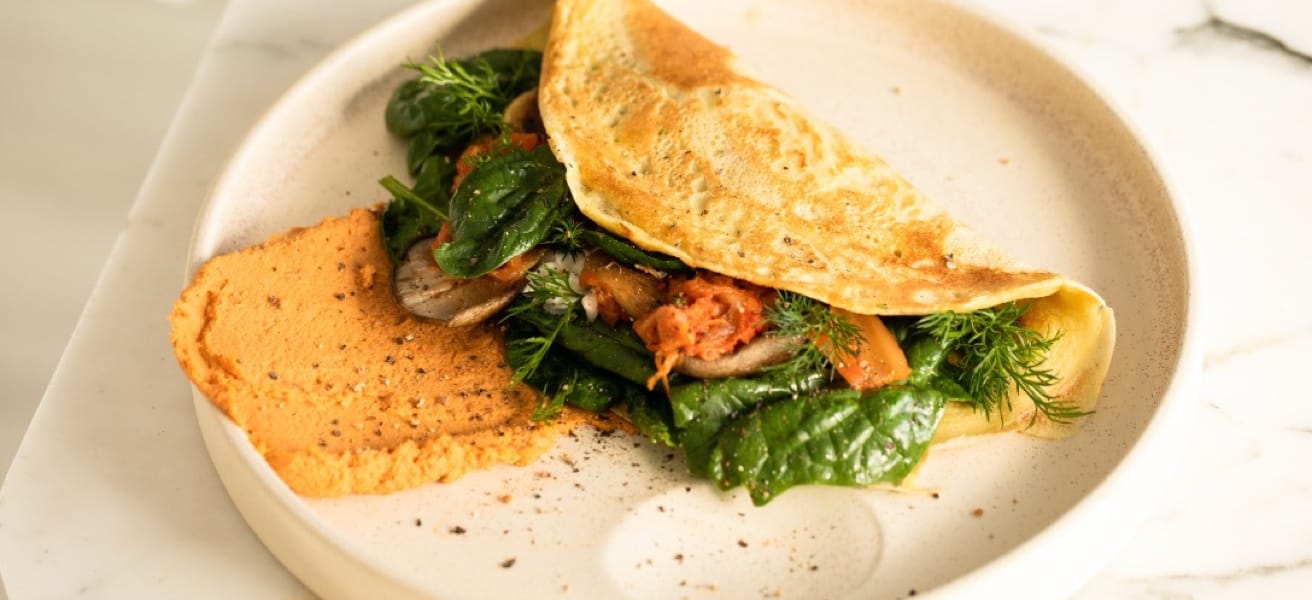 A folded omelet filled with leafy greens and vegetables on a white plate.